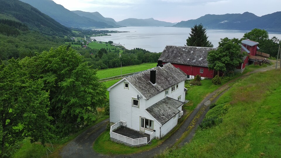 Det kvite gardshuset på Øggarden med fjorden og fjella i bakgrunnen